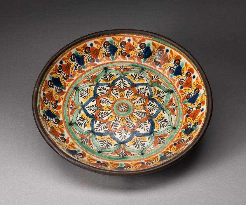 Glazed earthenware plate decorated with stylized leaves and flowers in red, yellow, green, dark blue, and white.