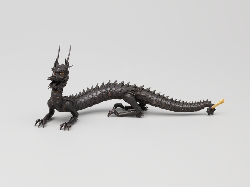 Small iron sculpture of a dragon with a serpentine body, legs with talons, and long tail, all made of moveable joints.