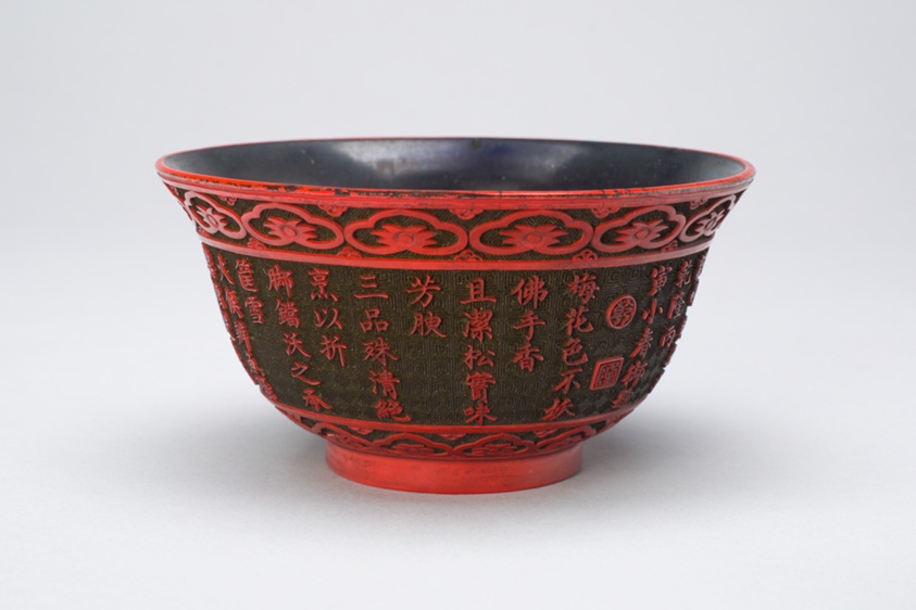 Black bowl with a narrow red base and embossed elements in red, including a floral border at top and bottom and Chinese characters in the middle.