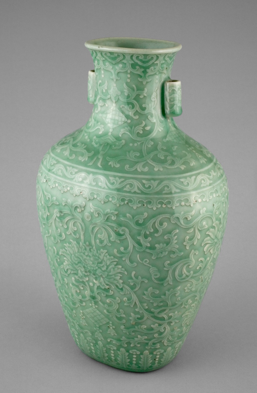 Green glazed vessel decorated with floral adornments, tapered and flared at the neck, with two small cylindrical handles.
