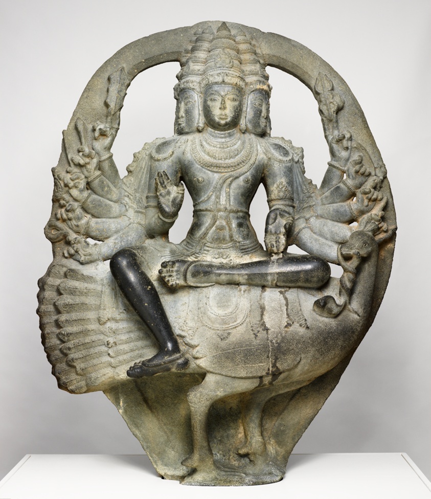Gray statue with multiple heads and arms seated on Peacock.