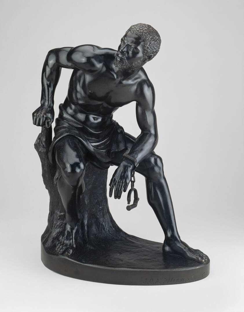 Black bronze statue of African American man, shackles broken, sitting on tree stump.