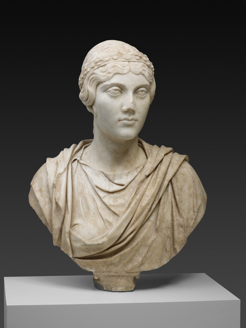 White marble bust of woman wearing headband and tunic.