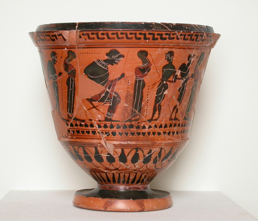 Bowl-shaped terracotta vessel with a foot, glazed in red with black figures encircling its body.