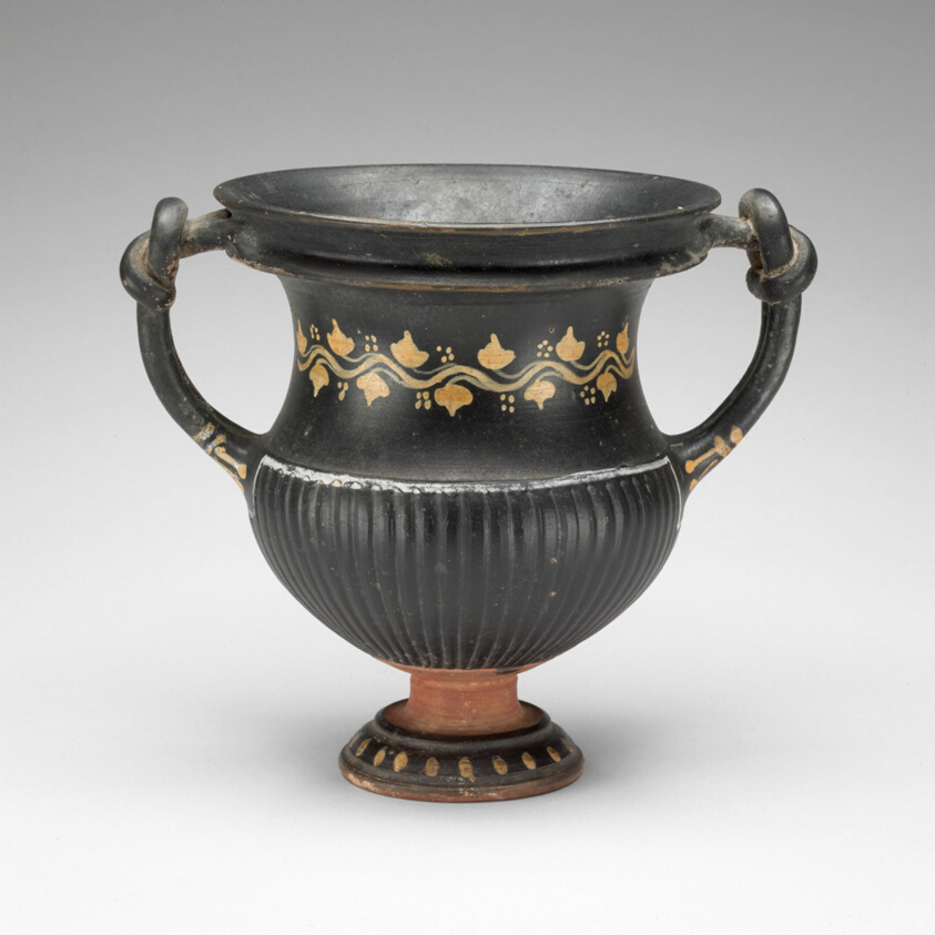 Terracotta cup with handles that appear tied in knots, a simple design around the middle, and a fluted section at the foot.