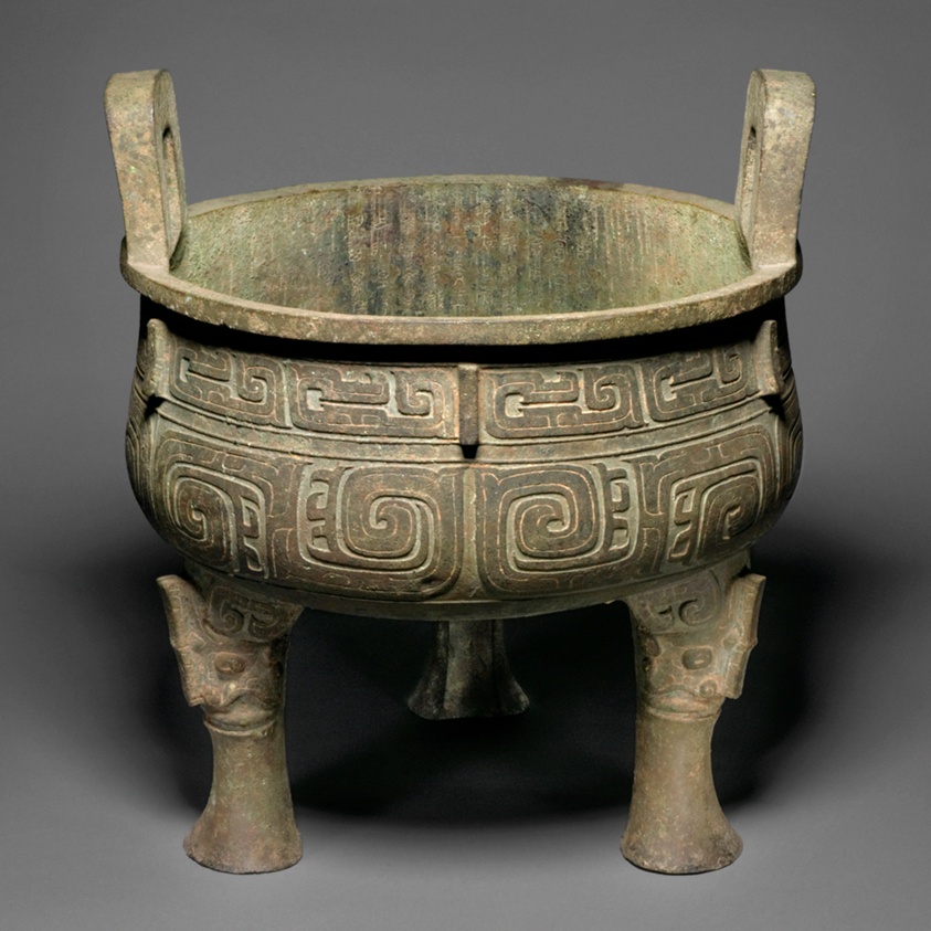 Medium sized cauldron with green patina, two handles, and three legs.