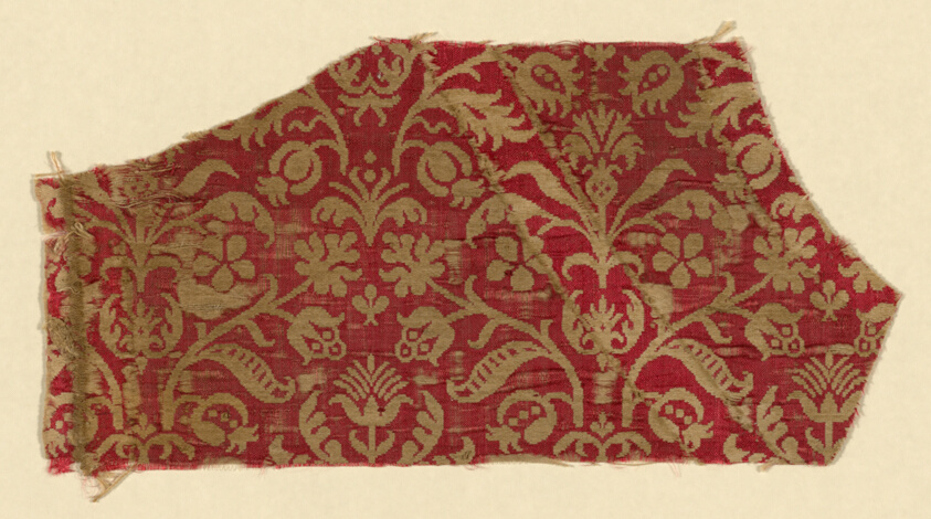 An irregularly shaped textile fragment of gold floral design on a red background.