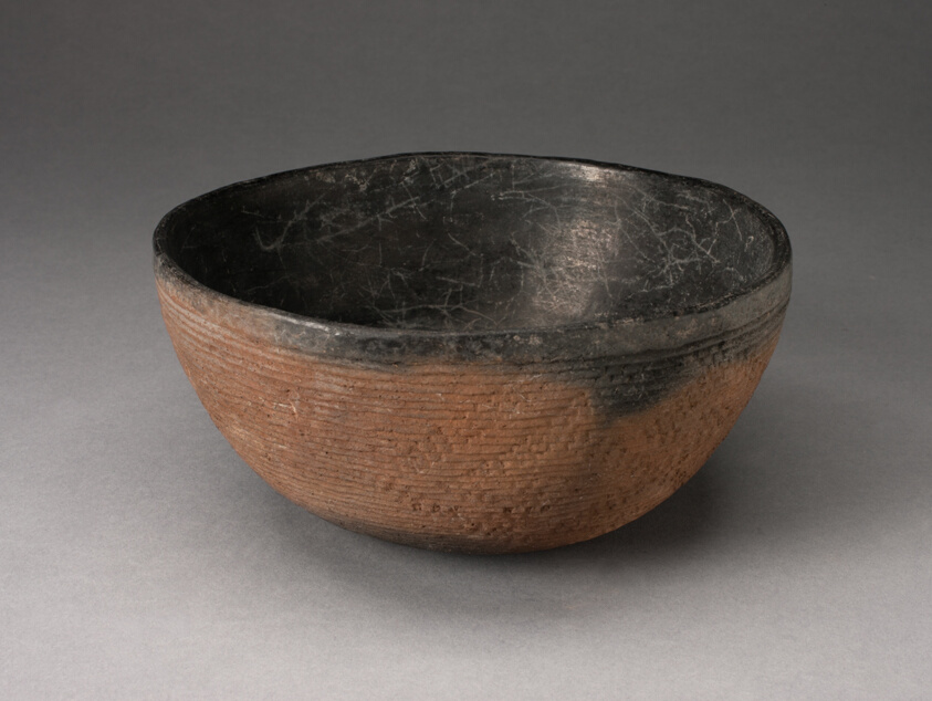 Round, red-brown bowl with small cracks its black interior. The outer surface is striated with tight horizontal lines and a diagonal pattern.