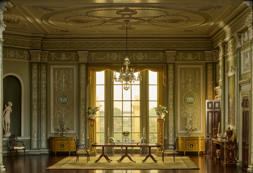 Miniature Georgian-era dining room with pale green walls, ornate white trim, long glass table.