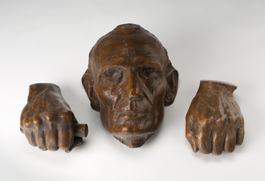 Three-part bronze sculpture set of two clenched hands and a man's face with closed eyes and mouth, an object in one hand.