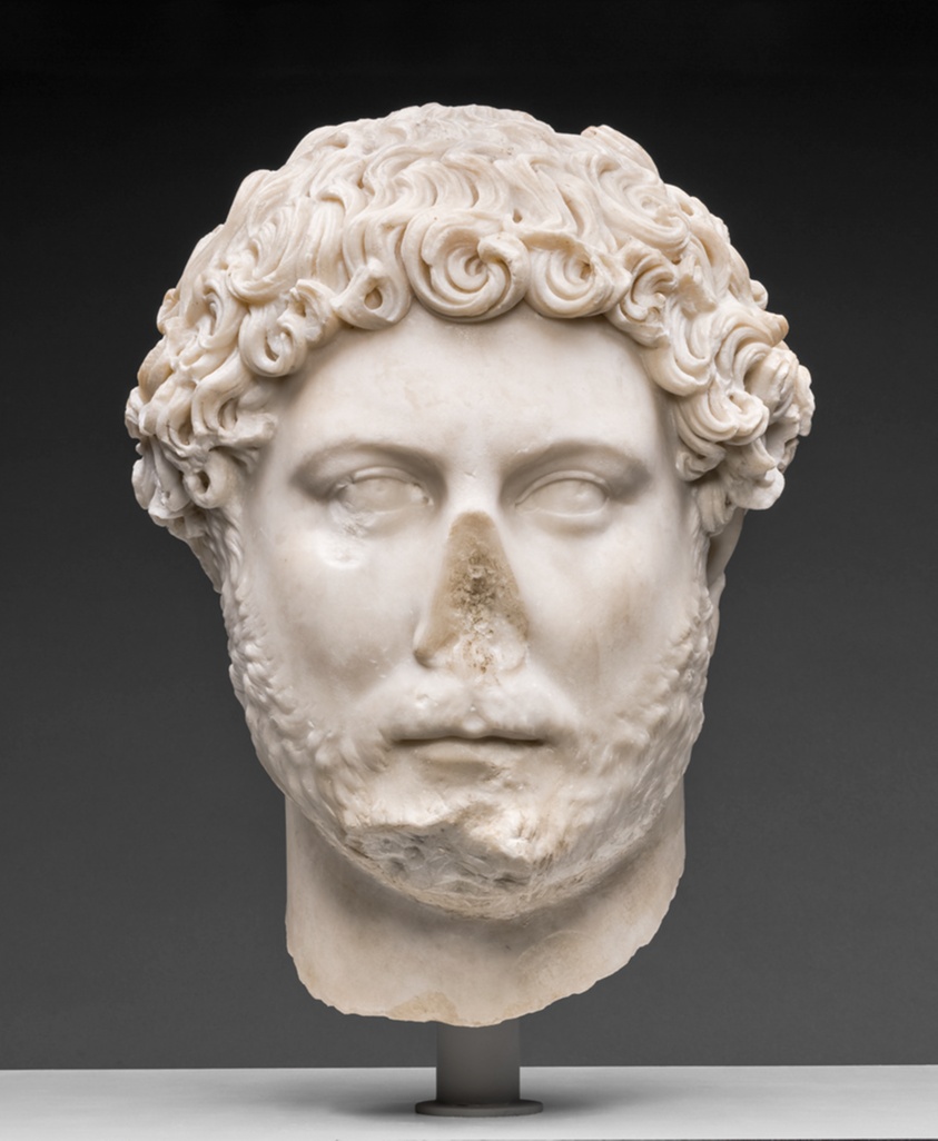 The white head of a man with a blank expression, a missing nose that has broken off, low cheekbones, curly hair, and a close-cut wavy beard.