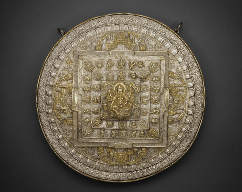 Plate sized sculpture depicting seated deity, adorned with figures, filigree, and temples.
