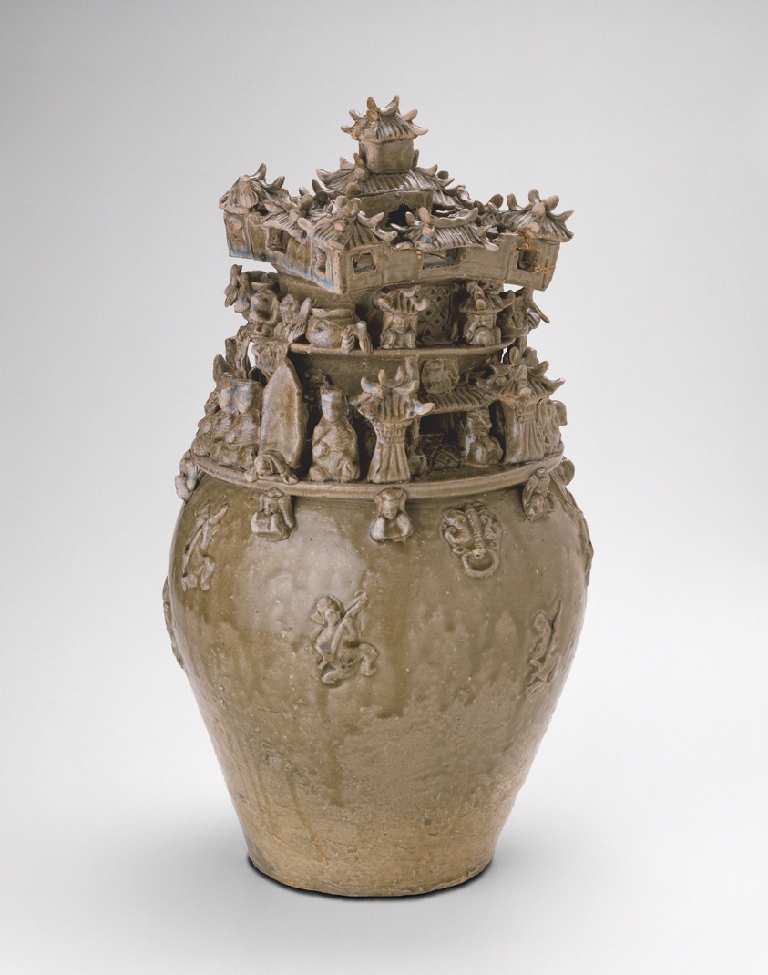 Medium sized olive colored urn, upper half carved into figures and structures.