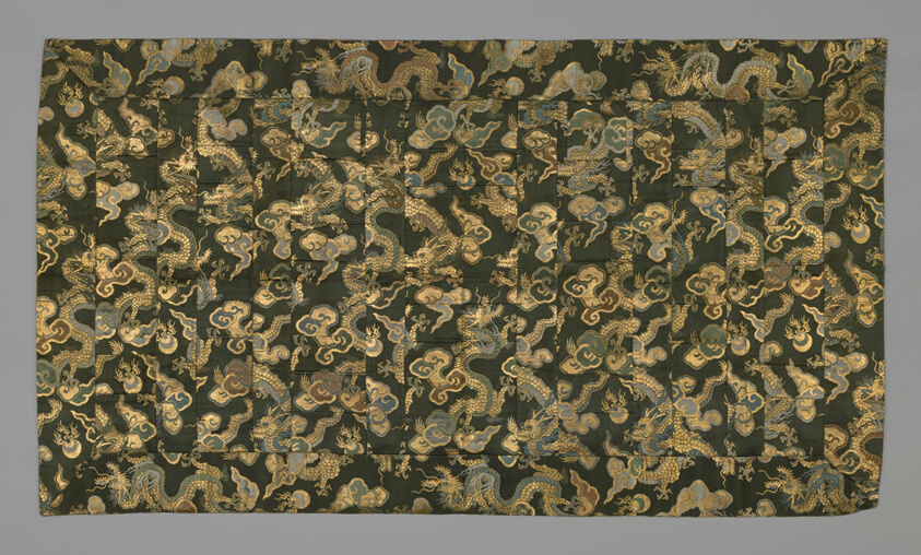 A rectangular garment of patchwork dark silk patterned with golden dragons and green, blue, and brown clouds
