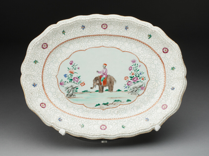 Porcelain oval platter with molded scalloped edge lavishly decorated with white floral pattern with colorful elements. The central scene depicts an elephant with a rider flanked by brightly-colored flowers.