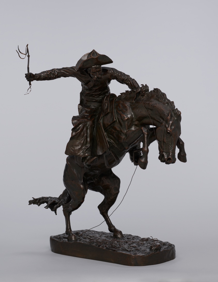 Brown bronze statue of man with riding crop atop a rearing horse.