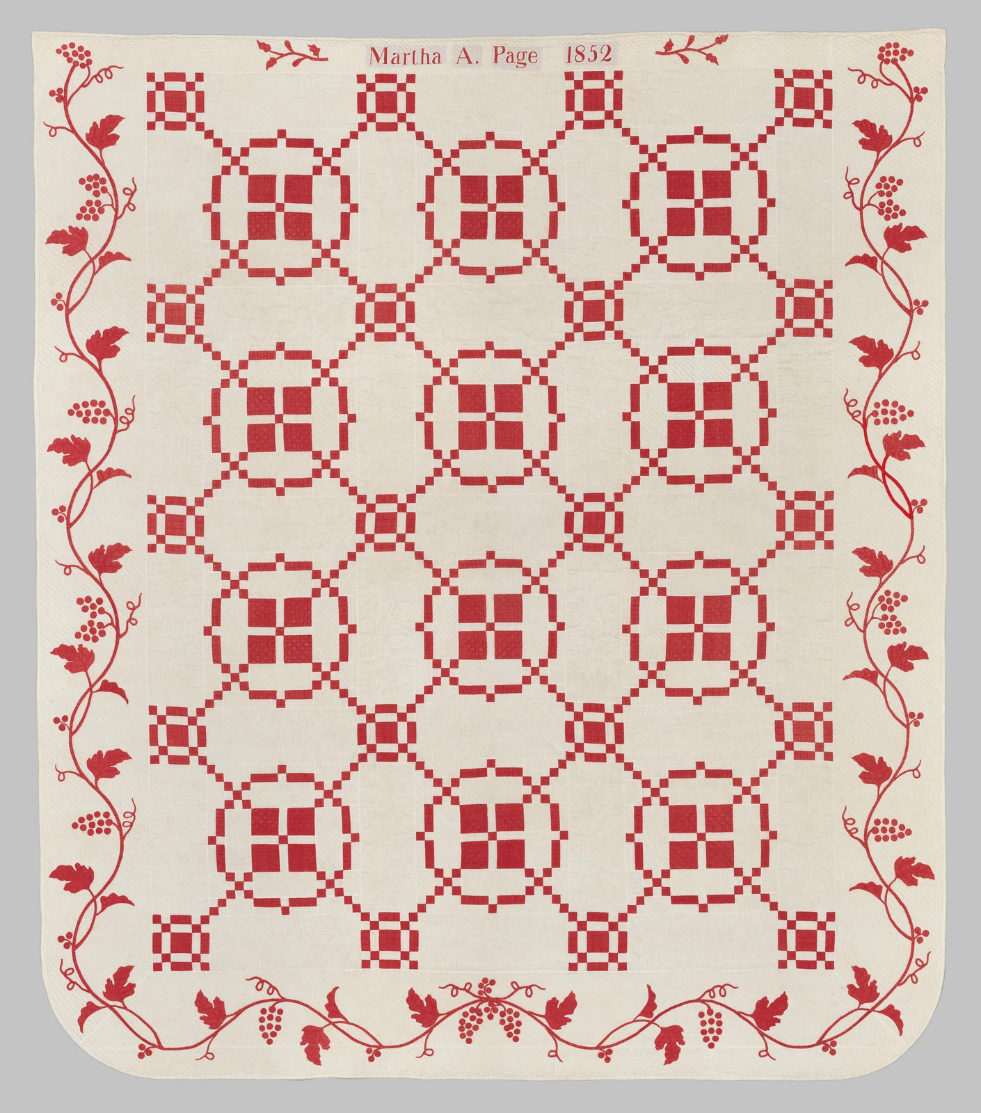 Small red and white squares form a repeating lattice across a cotton quilt.